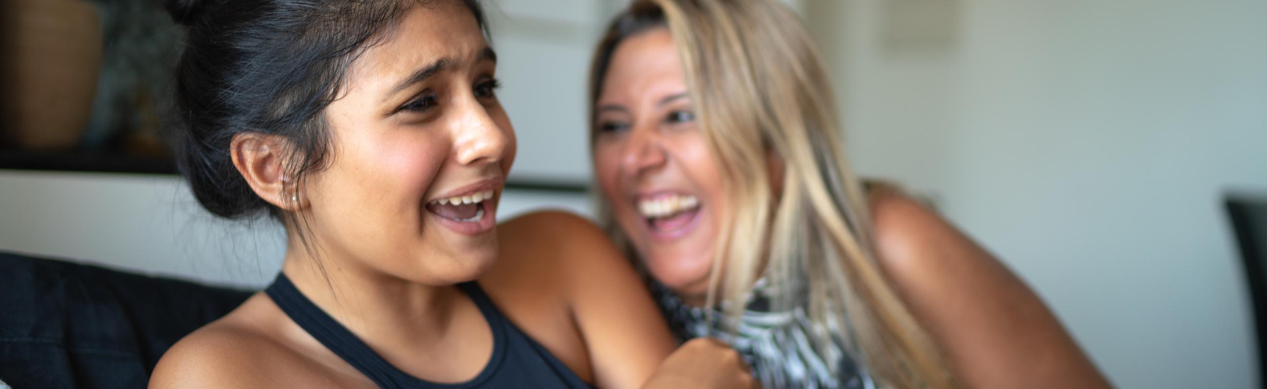 a mother and daughter laugh while sitting on a couch
