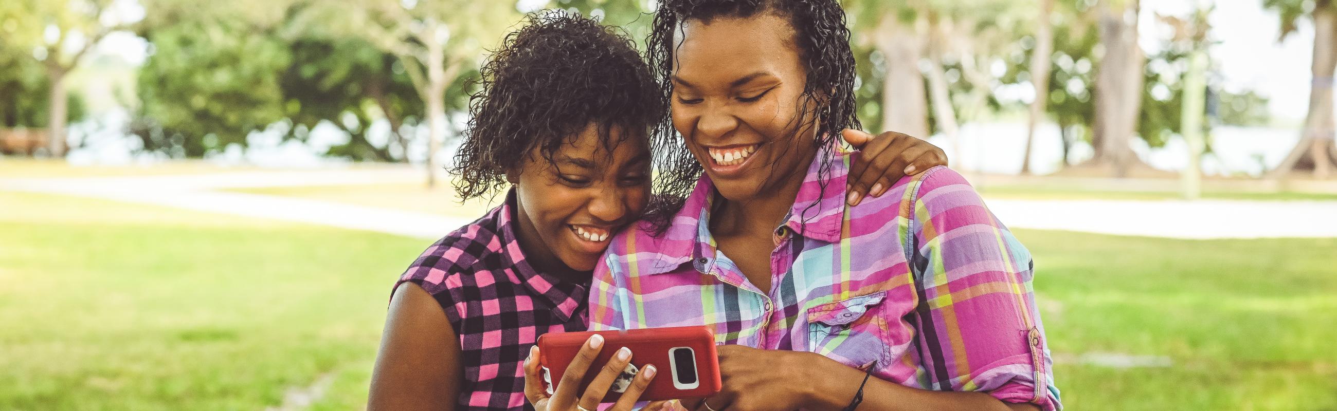 a mom and daughter laugh while looking at a phone